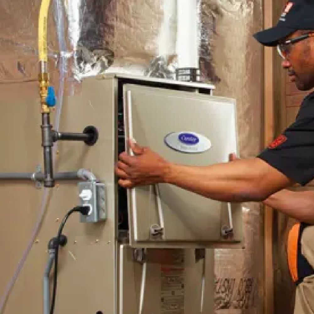 HVAC technician opening a furnace panel. Furnace is beige. Wall is insulated.