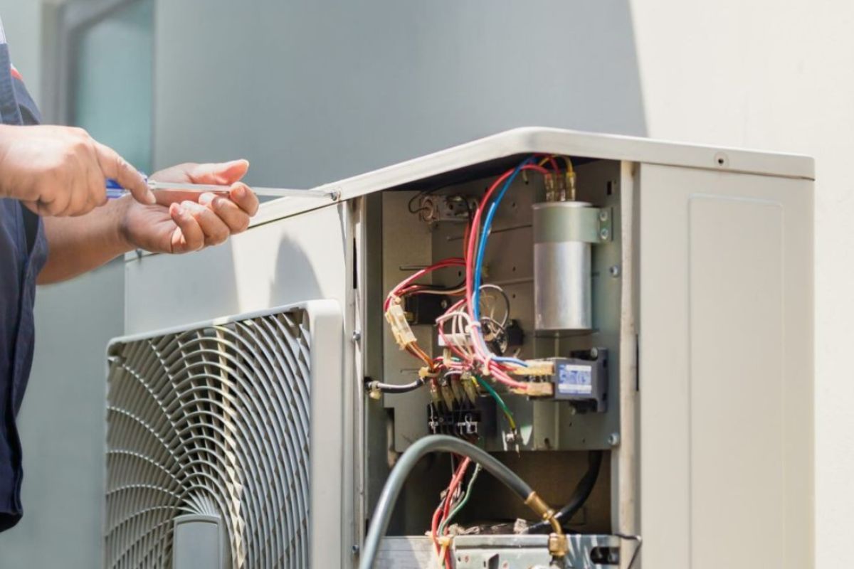 HVAC technician repairs an outdoor air conditioning unit with open access to the electrical components.