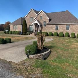Suburban brick house with curved driveway, trimmed shrubs, and a landscaped front yard