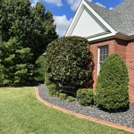 Brick house with white gable, manicured shrubs, and a mulched garden bed beside a green lawn.