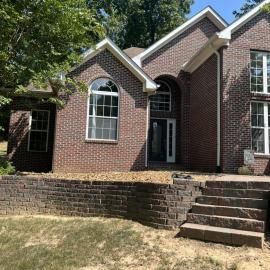 Brick suburban house with arched windows, front steps, and a raised lawn wall under sunny skies