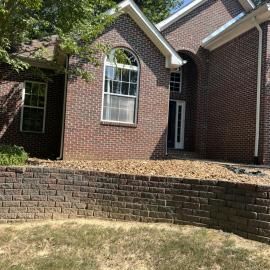 Brick house exterior with arched window, front entry, and a low retaining wall along the yard