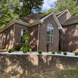 Brick suburban house with arched windows, sloped roof, and a stone retaining wall in front