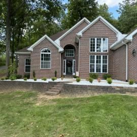 Brick suburban house with large windows, front porch, and landscaped lawn under trees