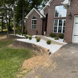 Brick house front entrance with white gravel landscaping, shrubs, and sloped driveway.