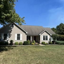 Suburban single-story house with gray siding, white trim, and a large front lawn under a blue sky