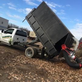 Tow truck lifting a tipped black dump truck on a muddy lot under a blue sky