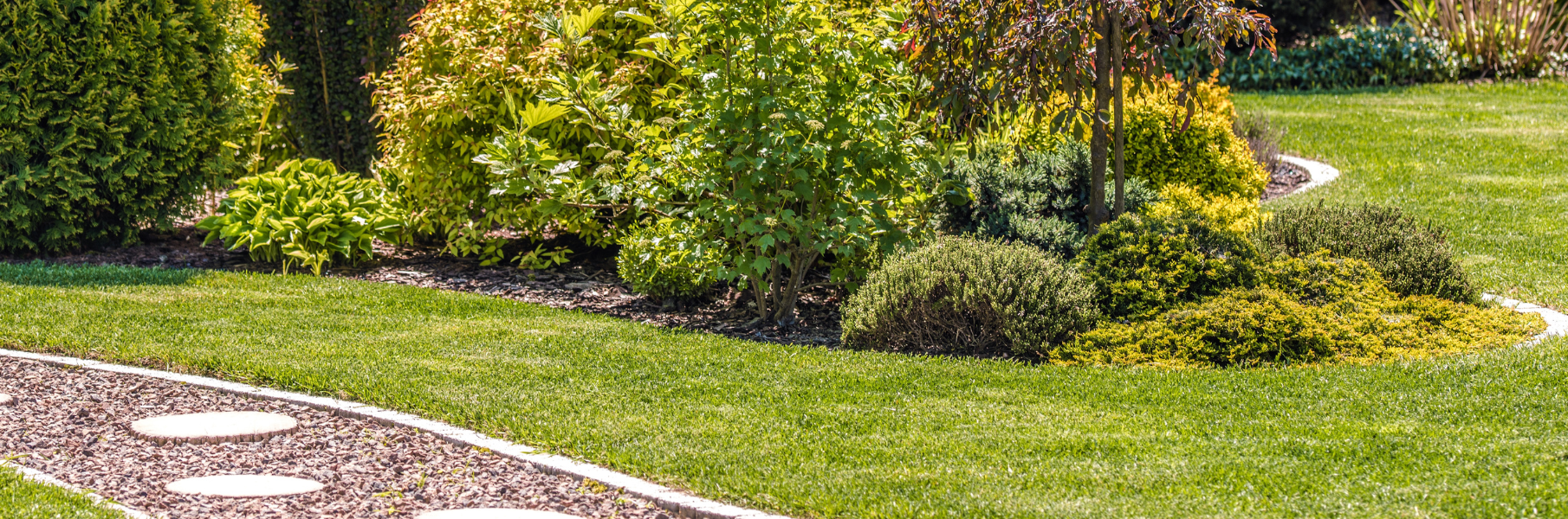 Landscaped garden with shrubs and flowers beside a curved stone path and green lawn