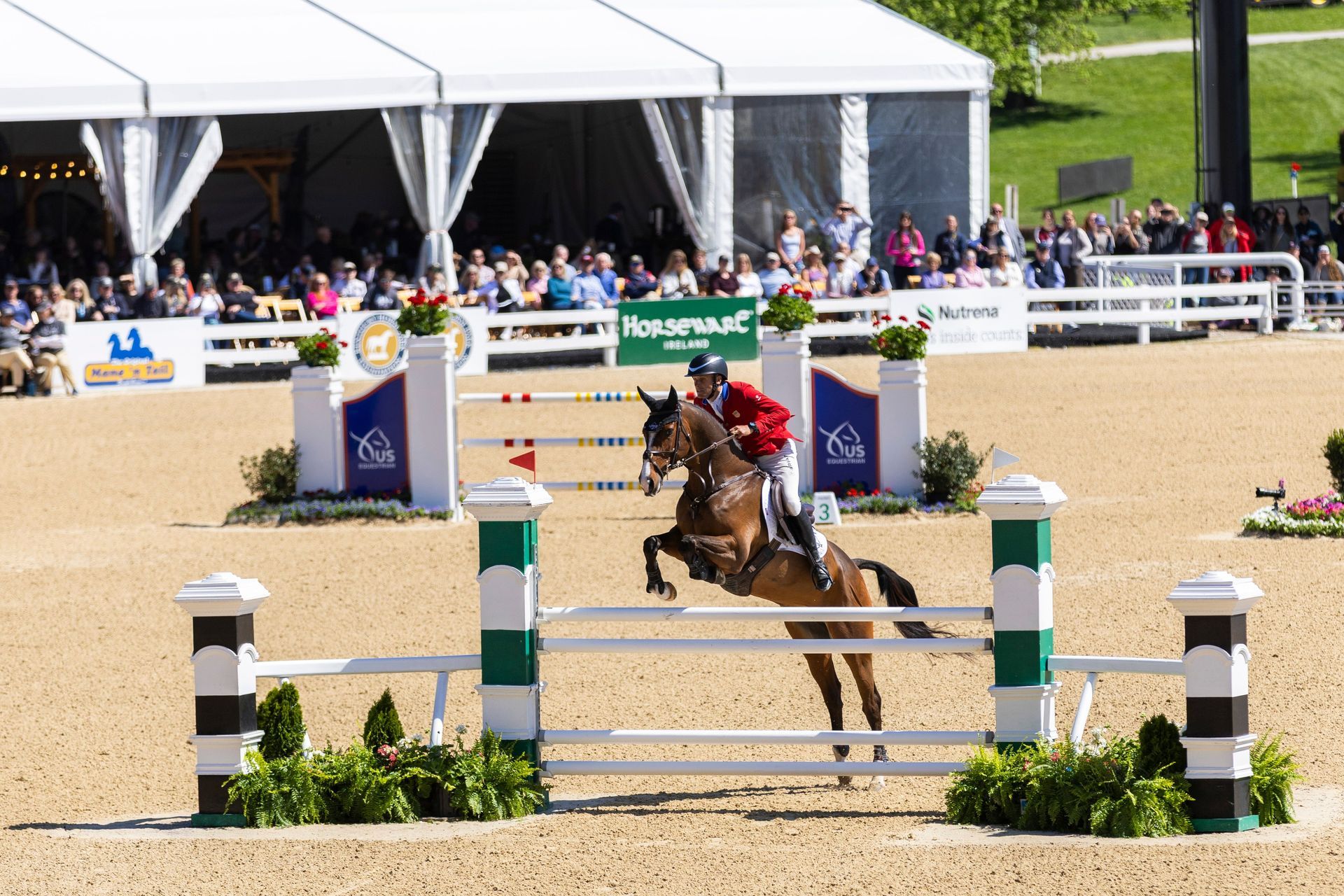 A horse and rider jumping in front of a crowd under hospitality tent