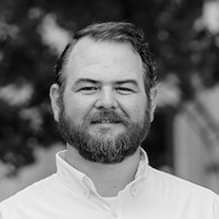 A black and white photo of a man with a beard wearing a white shirt.