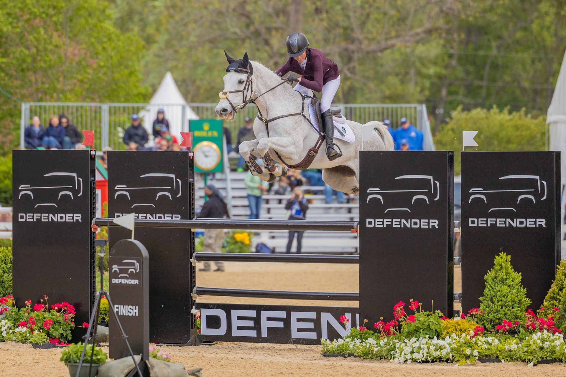 A man is riding a white horse over a fence.