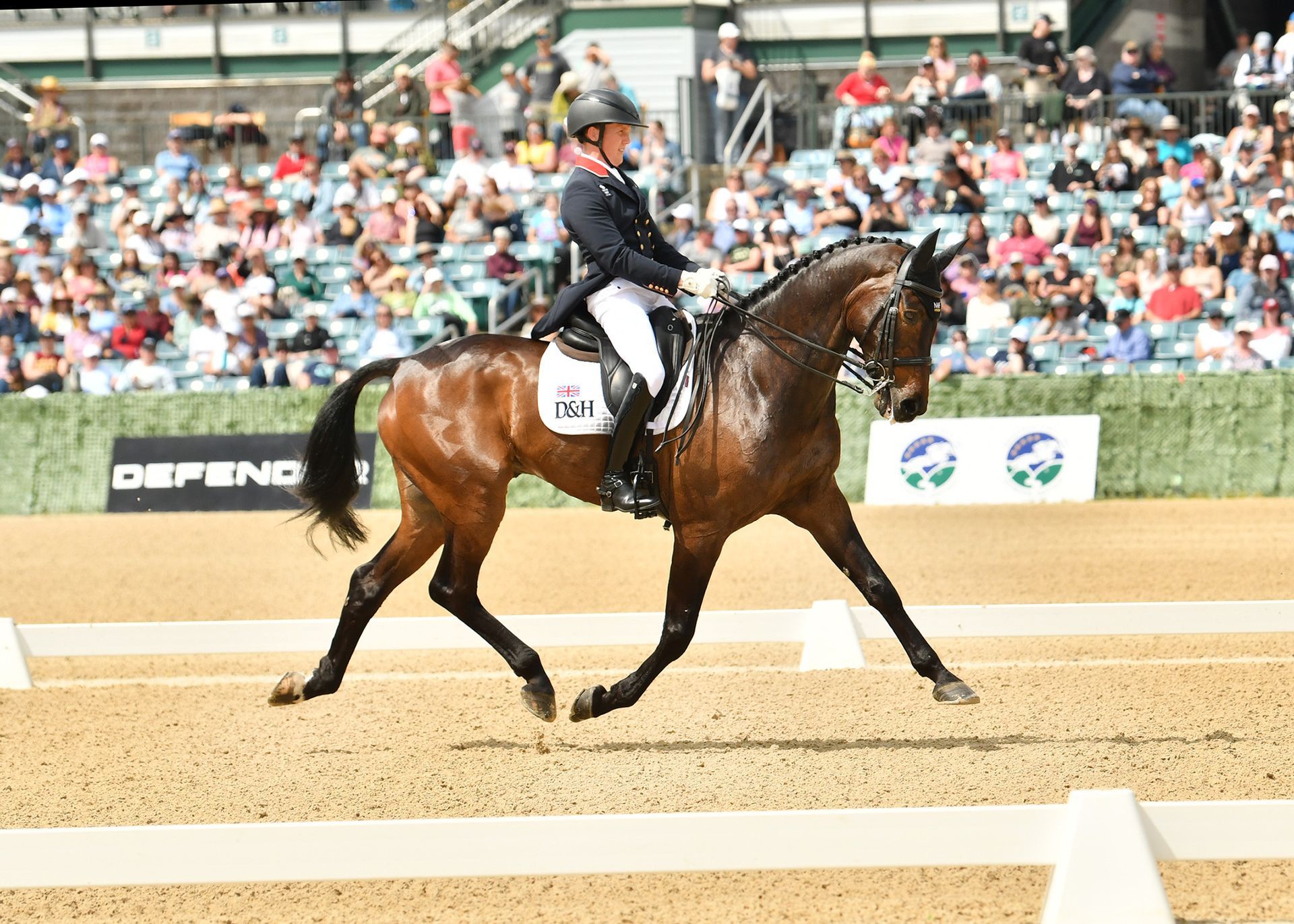 A woman is riding a brown horse on a dirt track.