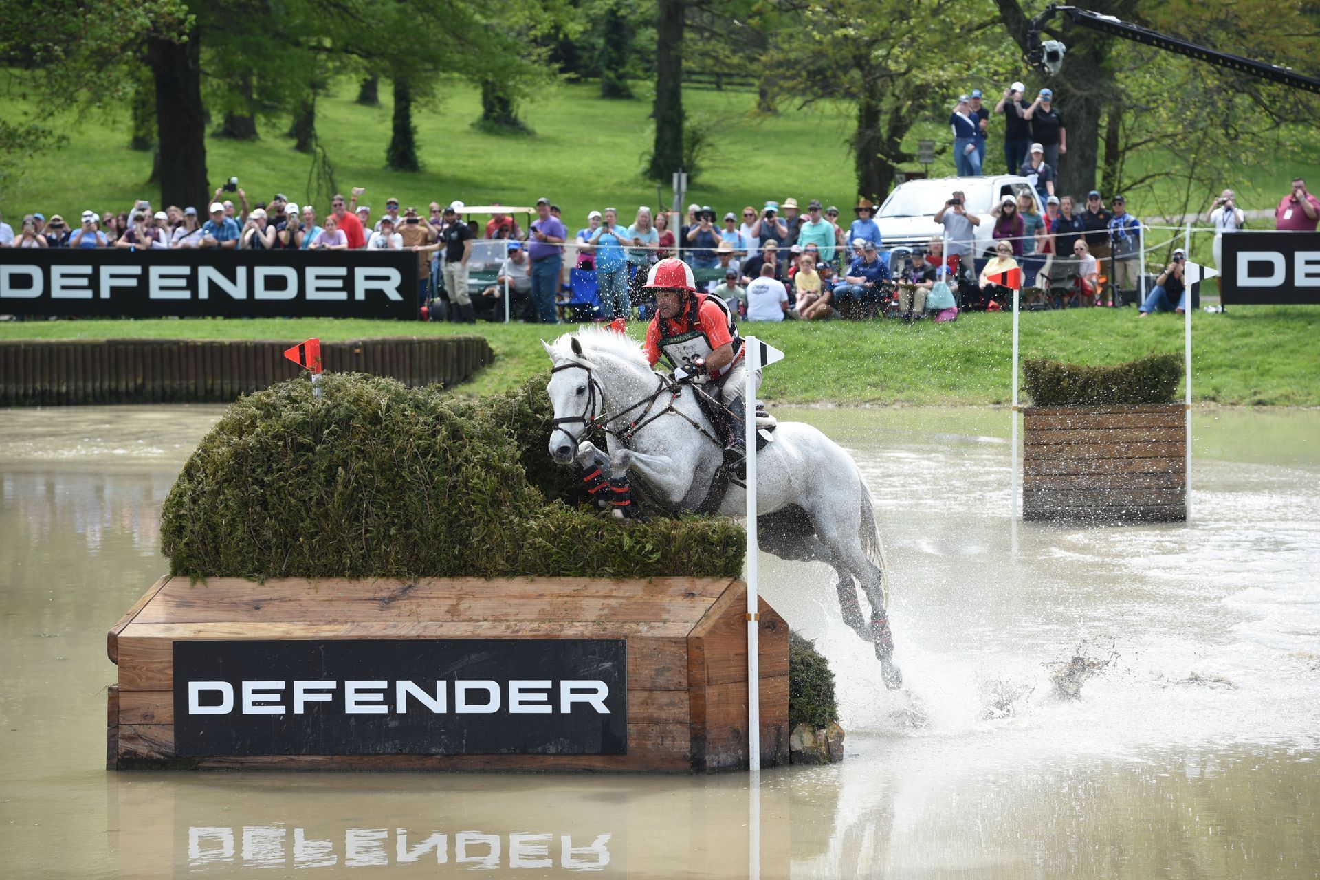 A person is riding a horse through a puddle in front of a sign that says defender