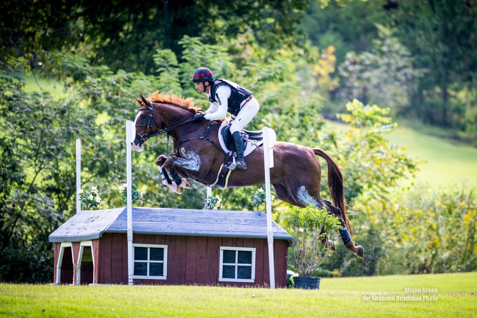 A person is riding a horse over a wooden fence.
