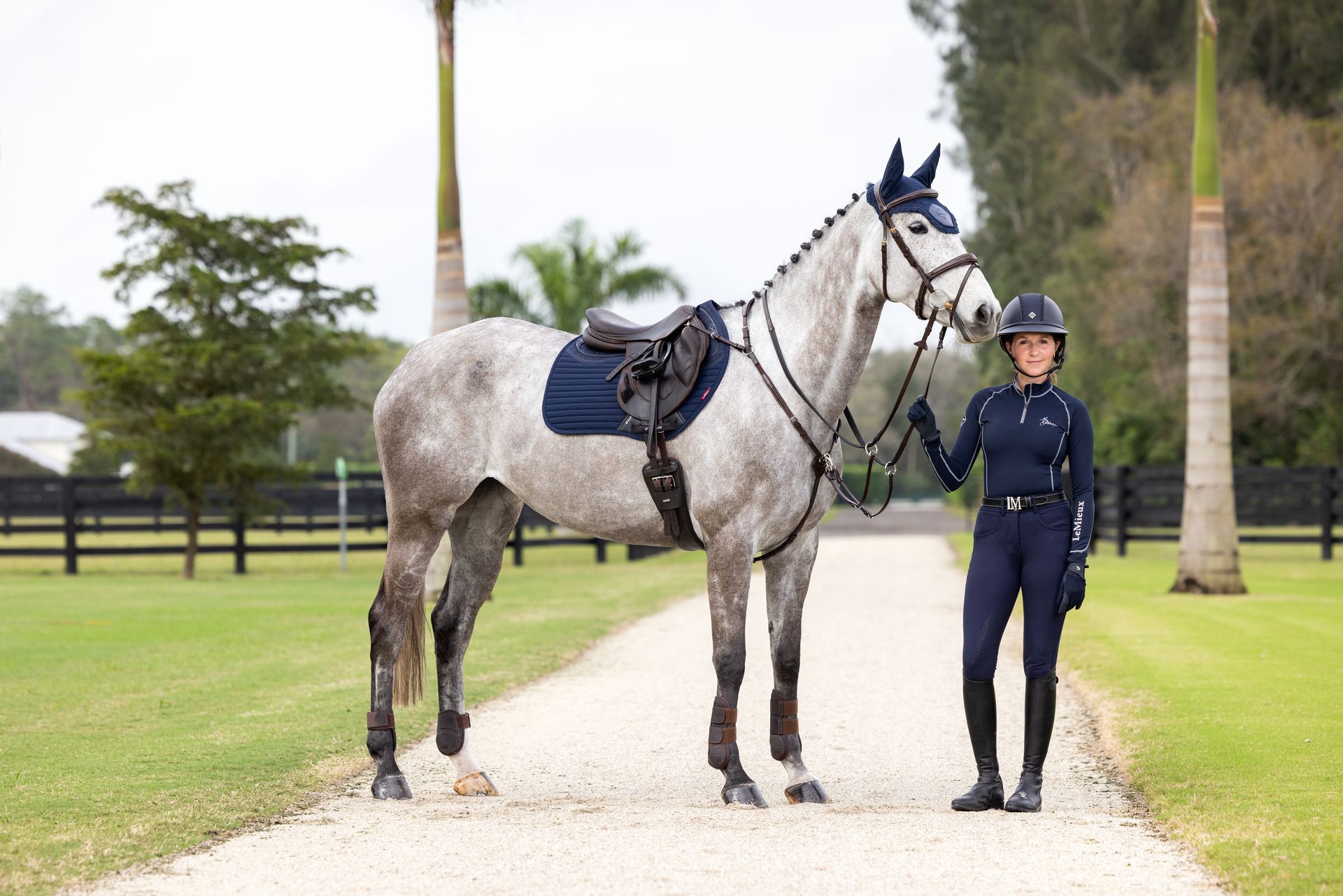 A woman is standing next to a horse on a dirt road.