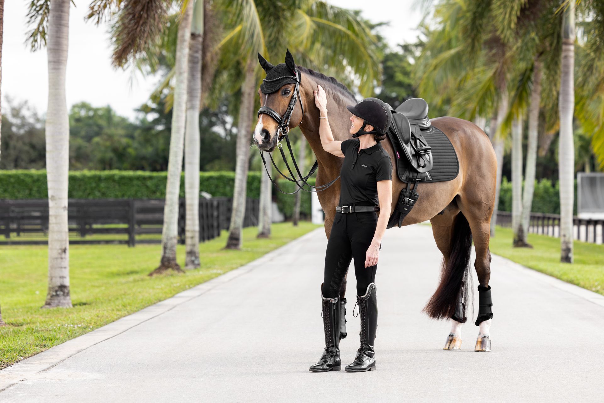 A woman is standing next to a brown horse on a road.