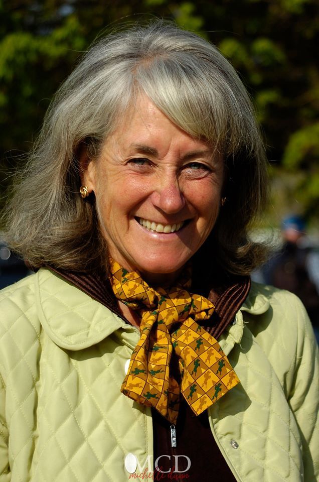 A woman wearing a yellow scarf and a green jacket is smiling