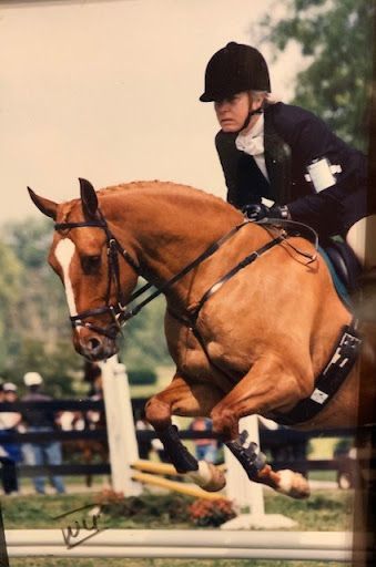A woman is riding a brown horse over a jump.