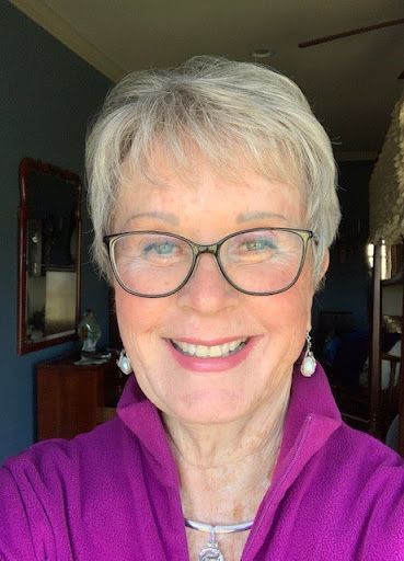 A woman wearing glasses and a purple shirt is smiling for the camera.