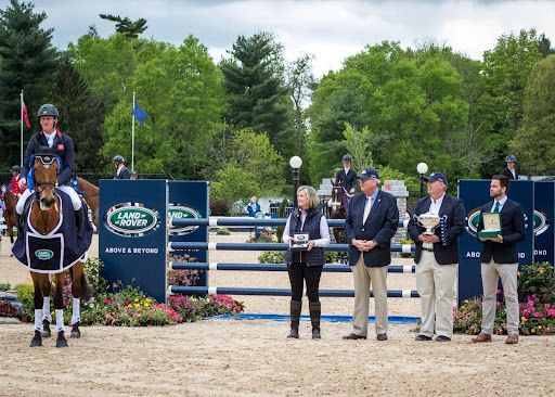 A woman is riding a horse in front of a group of people holding trophies.