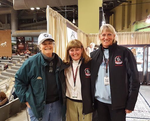 Three people posing for a picture with one wearing a jacket with a horse on it