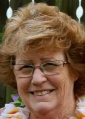 A woman wearing glasses and a lei is smiling for the camera.