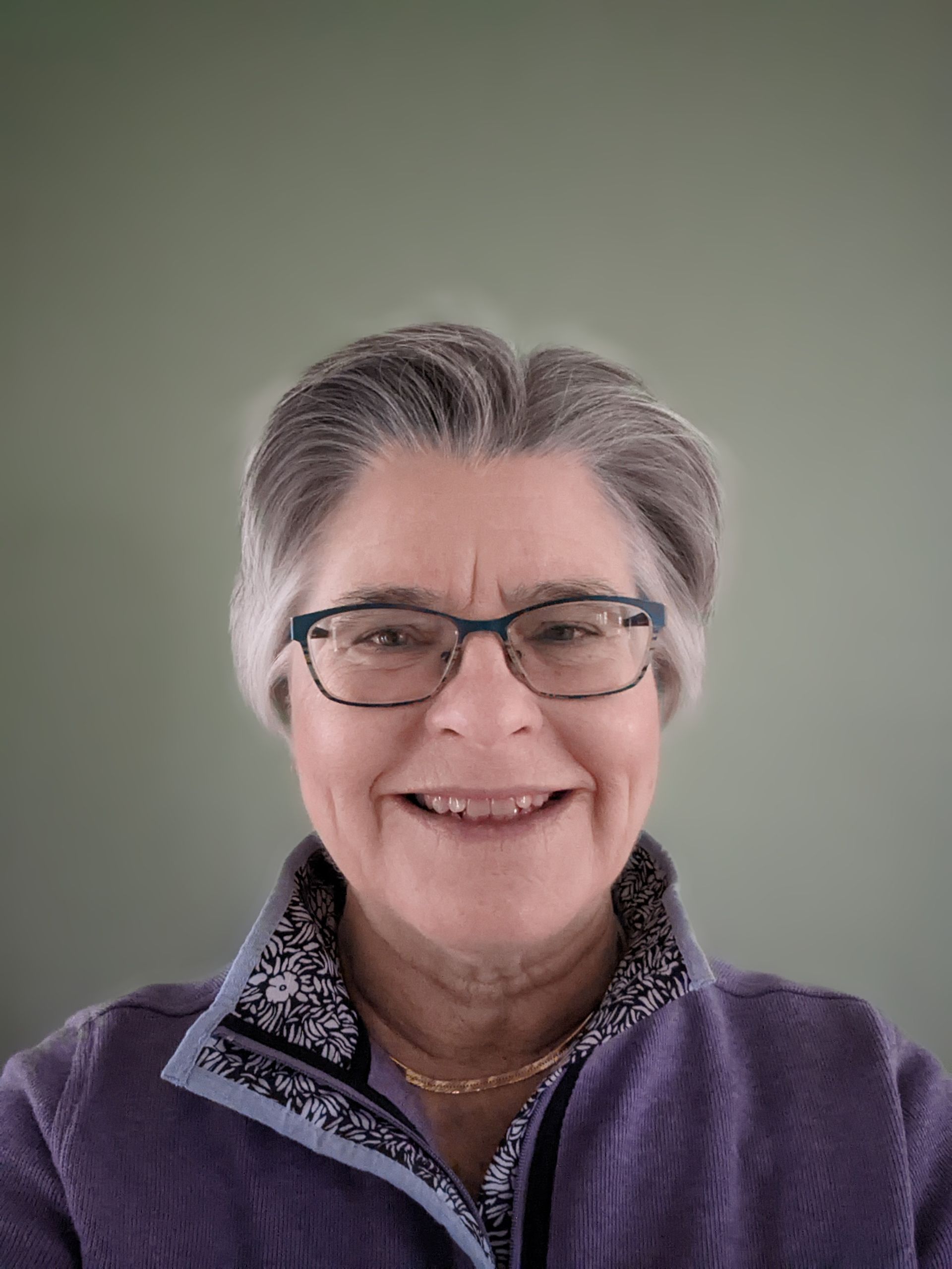 A woman wearing glasses and a purple jacket is smiling for the camera.