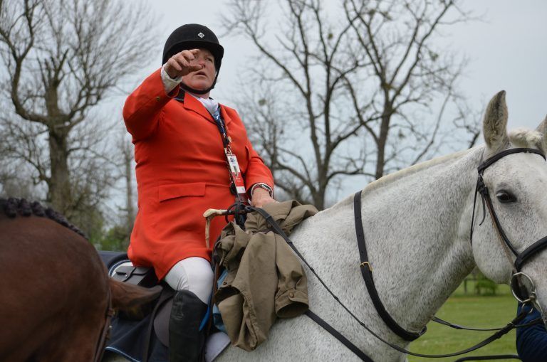 A woman in an orange jacket is riding a white horse.