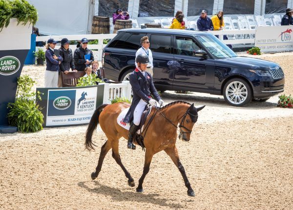 A man is riding a horse in front of a range rover.