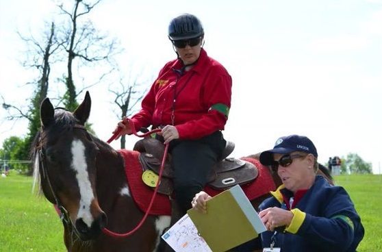 A woman in a red jacket is riding a horse