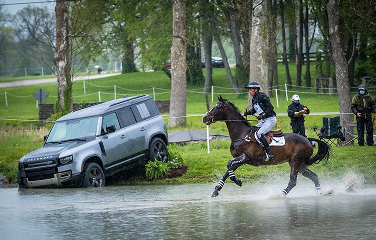 A man is riding a horse next to a car that has fallen into the water.