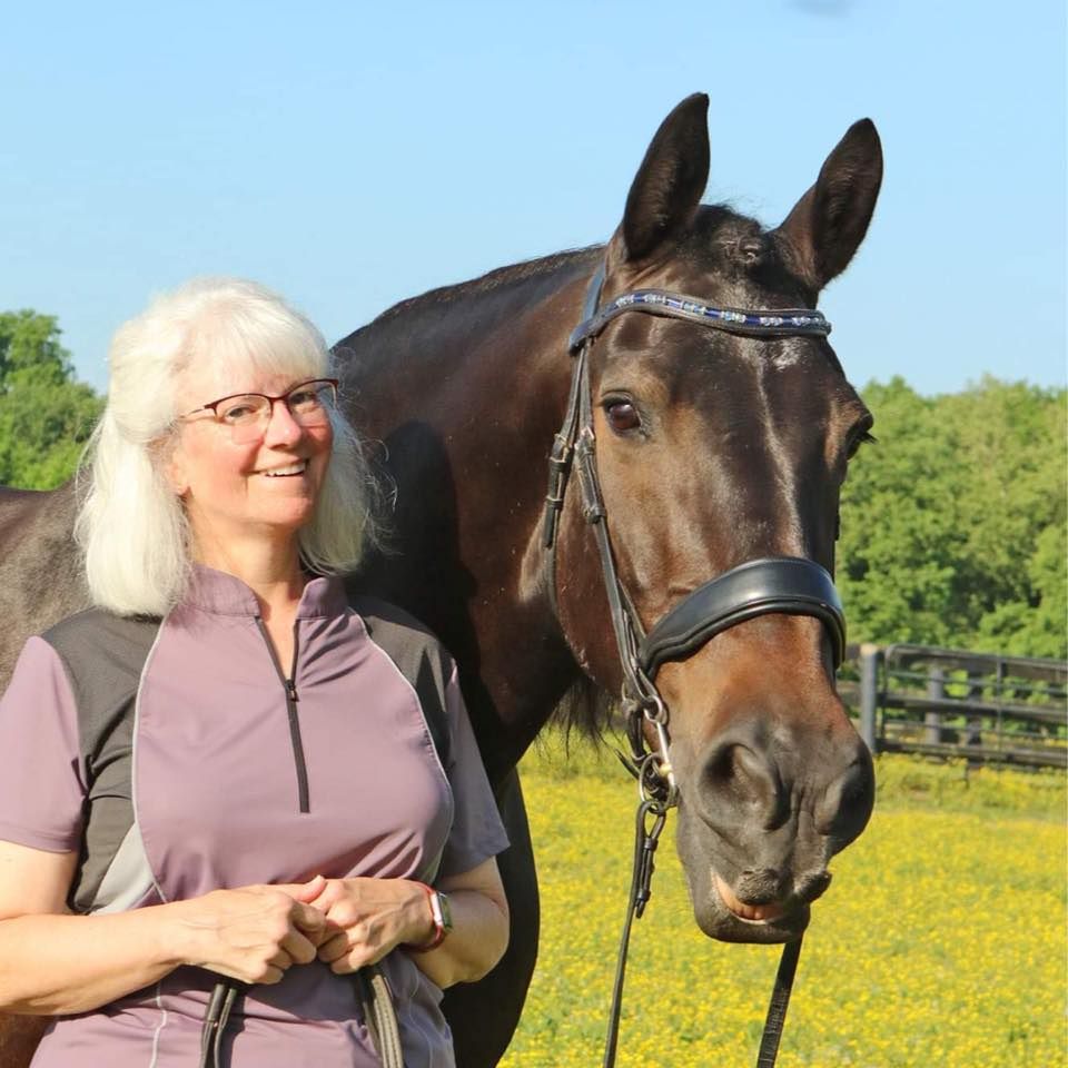 A woman stands next to a brown horse in a field