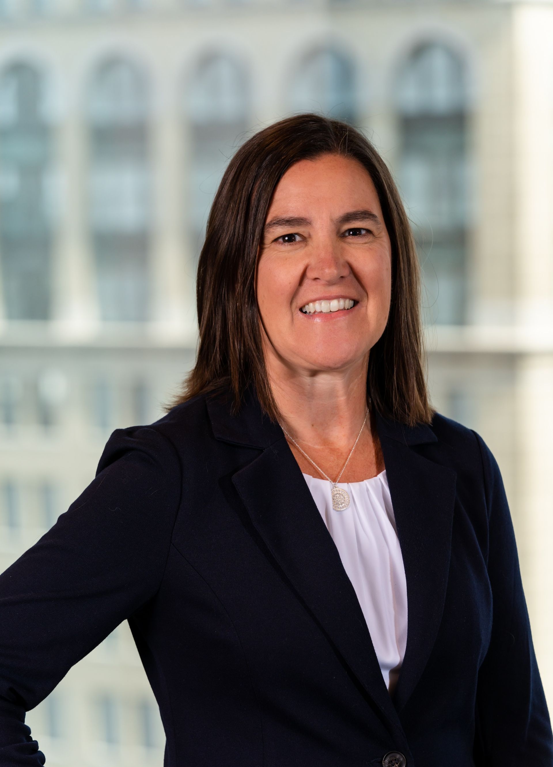 A woman in a business suit is smiling and standing in front of a building.