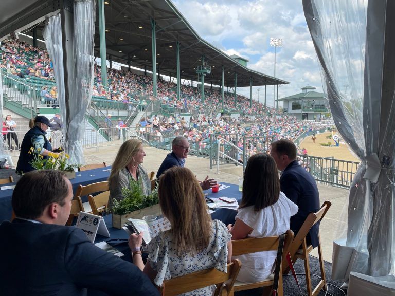 A group of people are sitting at a table in front of a stadium.