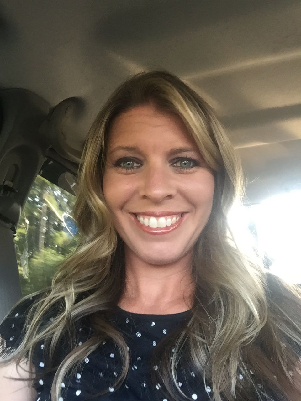 A woman is smiling while sitting in the back seat of a car.