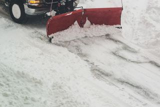 A red snow plow is plowing snow on a snowy road.