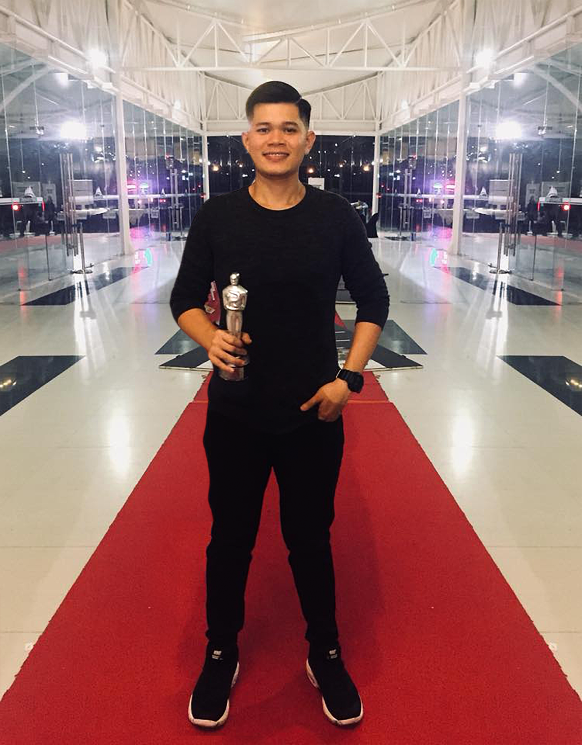 A man is standing on a red carpet holding a trophy.