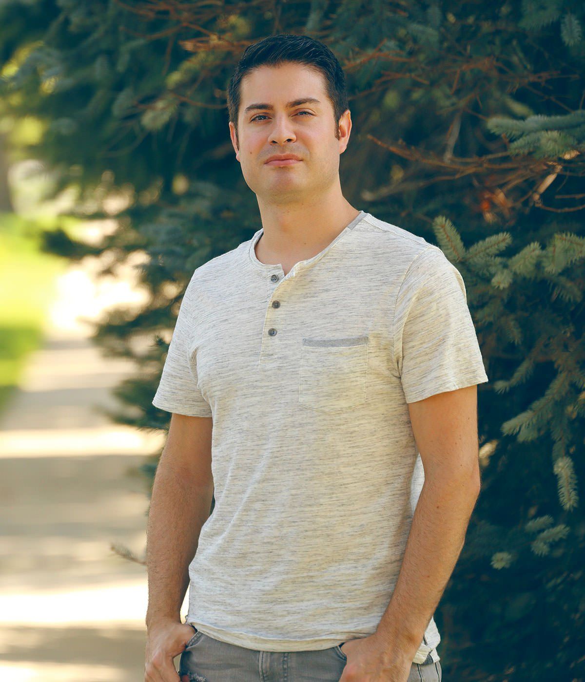 A man in a white shirt is standing in front of a tree.