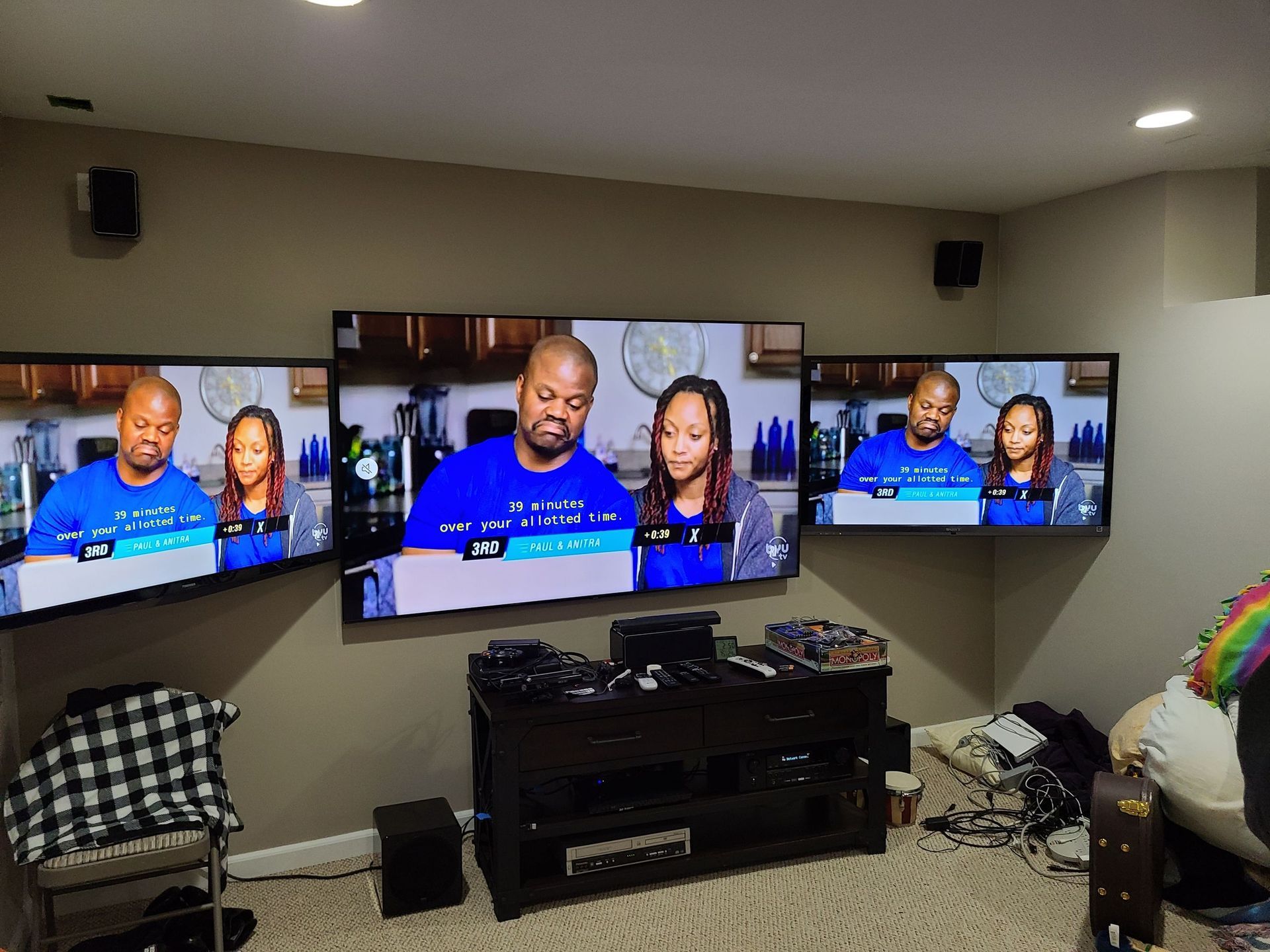 Three wall-mounted TVs in a living room display a news broadcast with two presenters by Audio Video Concepts