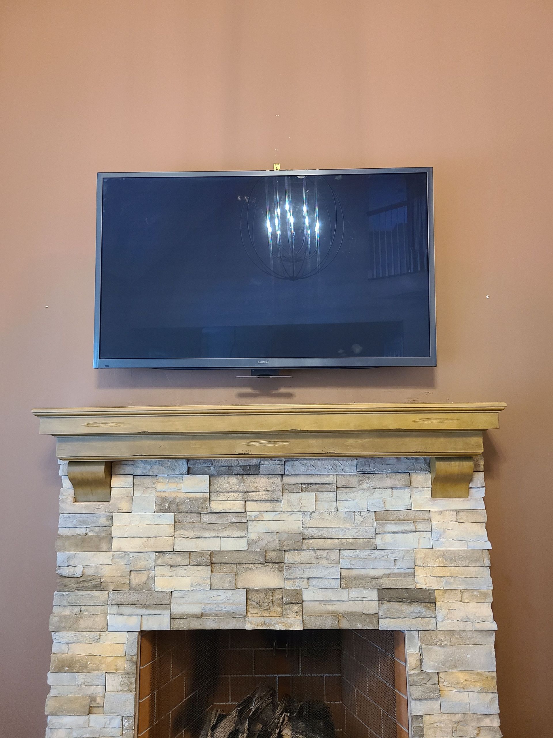 Flat-screen TV mounted above a stone fireplace mantel on a beige wall by Audio Video Concepts