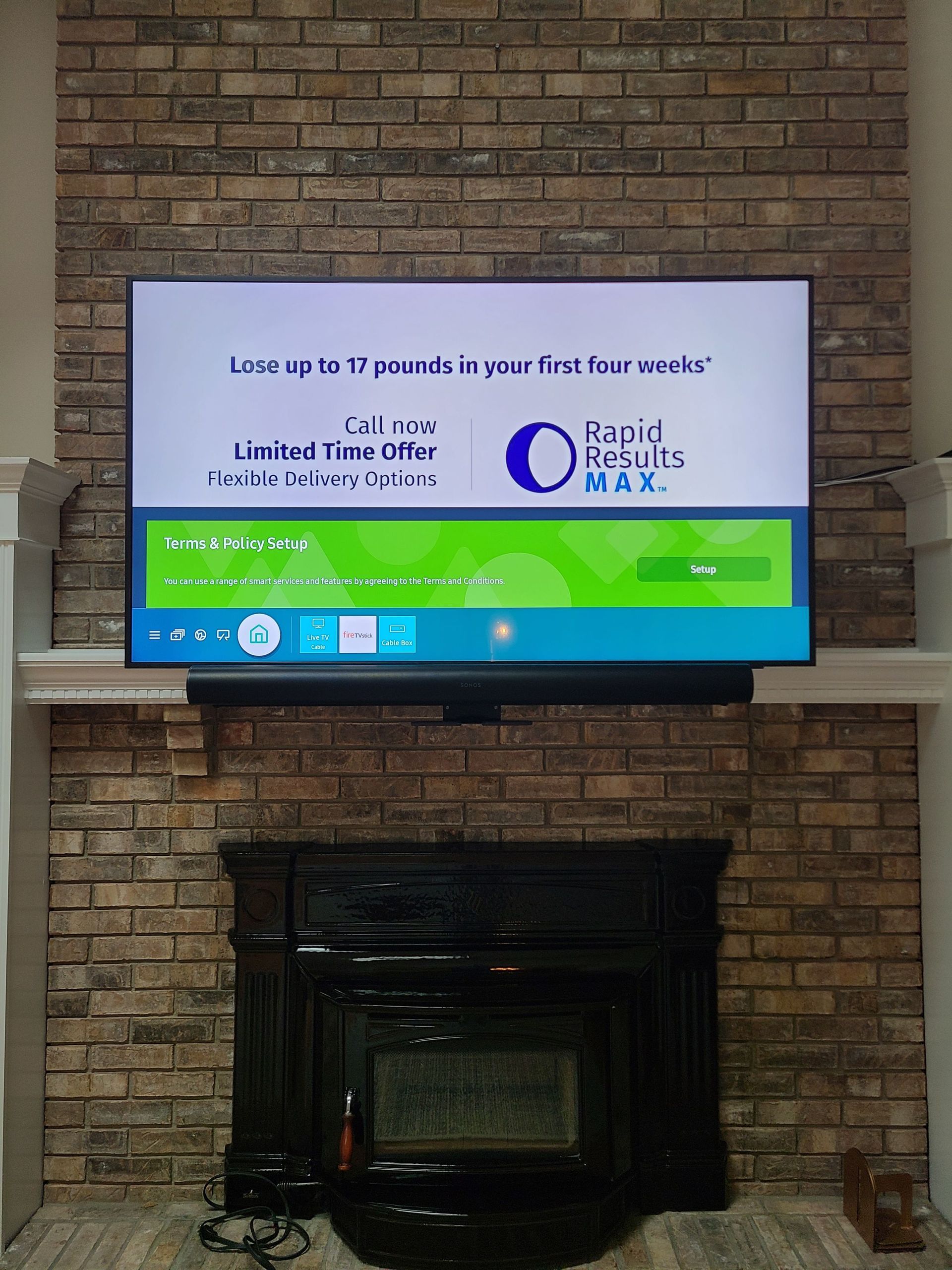 Wall-mounted TV in brick fireplace alcove displaying a colorful ad with text and a QR code by Audio Video Concepts