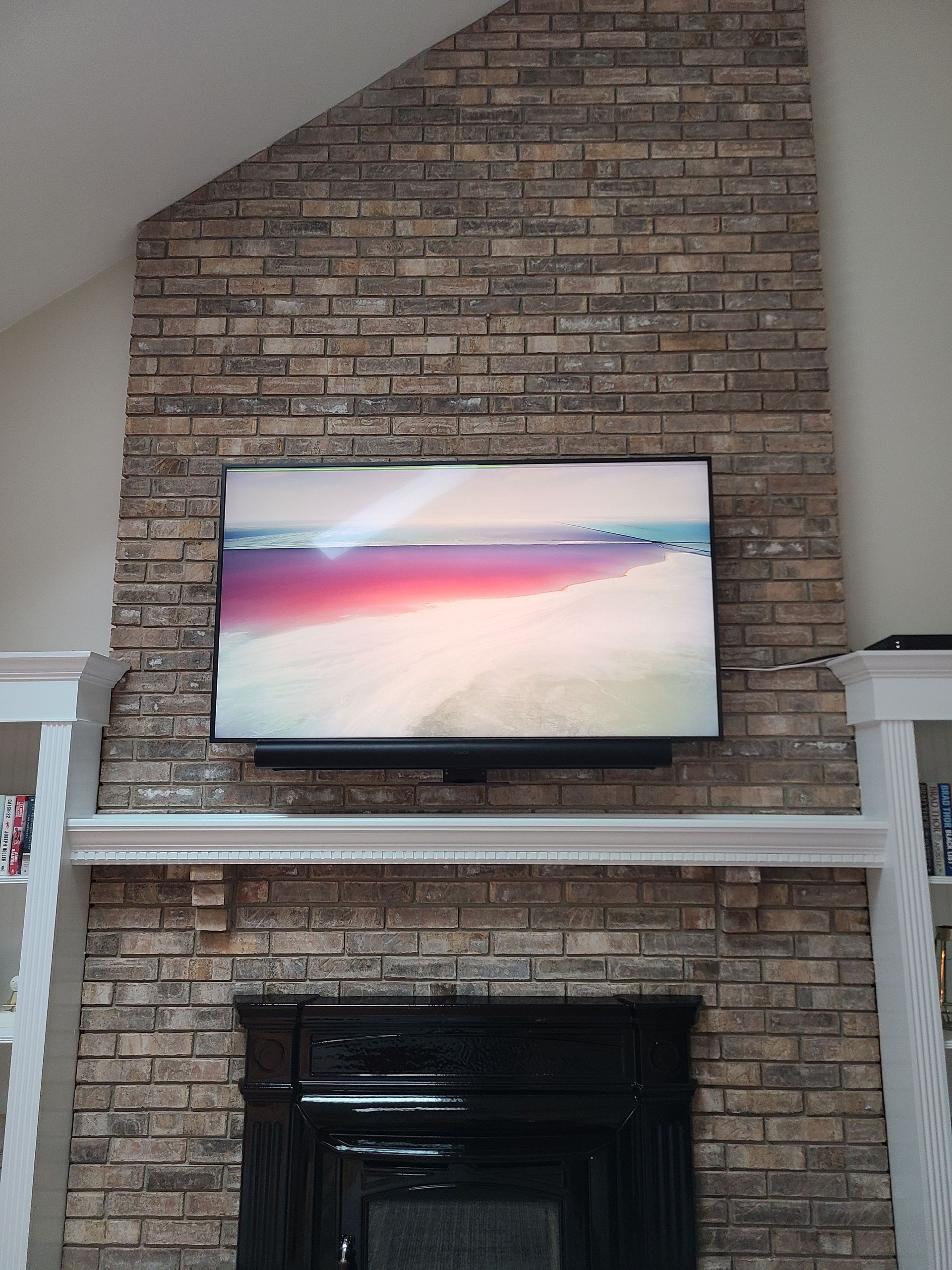 TV mounted above a brick fireplace in a living room with a beach scene on screen by Audio Video Concepts