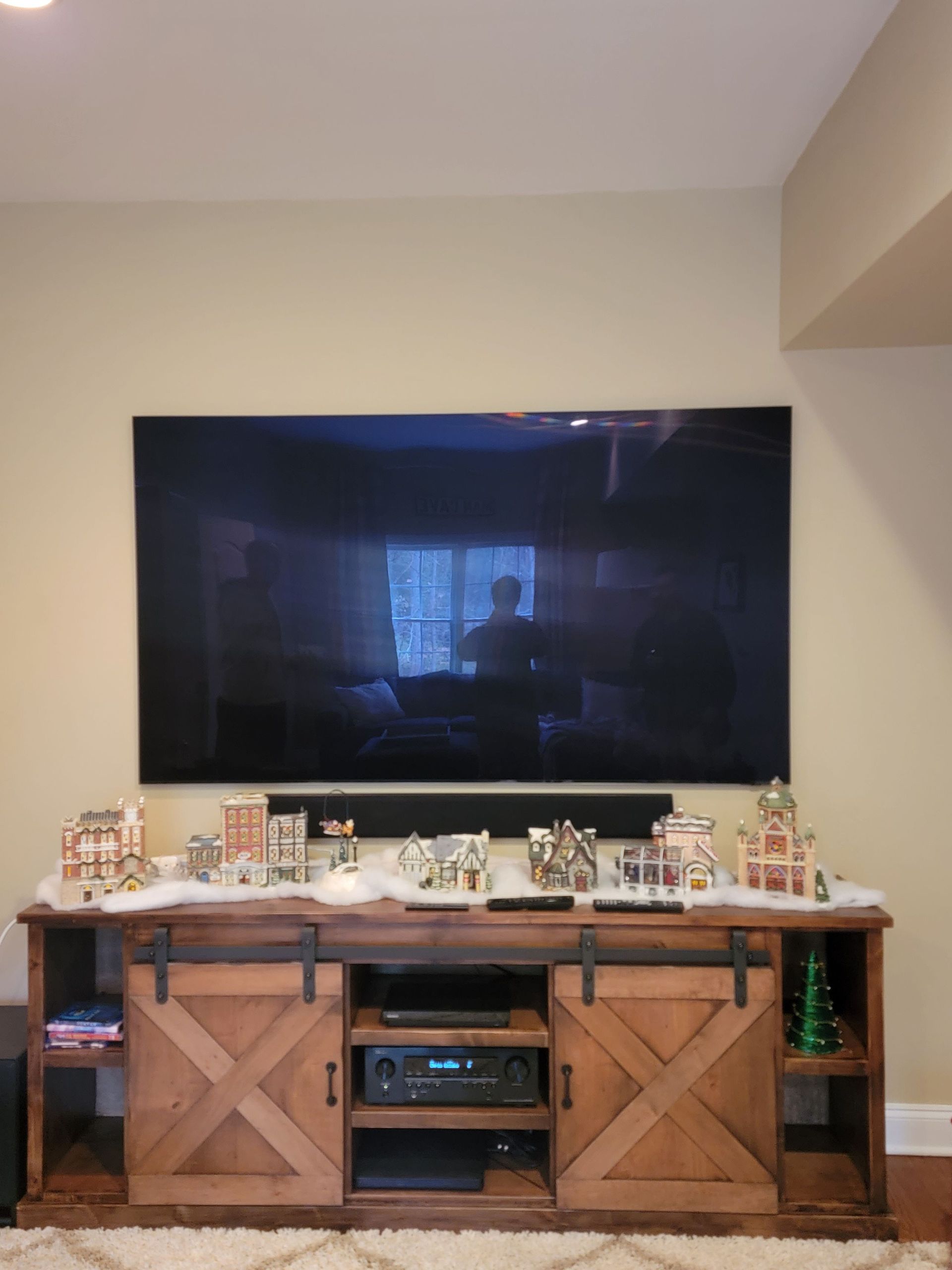 Large wall-mounted TV above a wooden console with holiday decorations in a living room by Audio Video Concepts