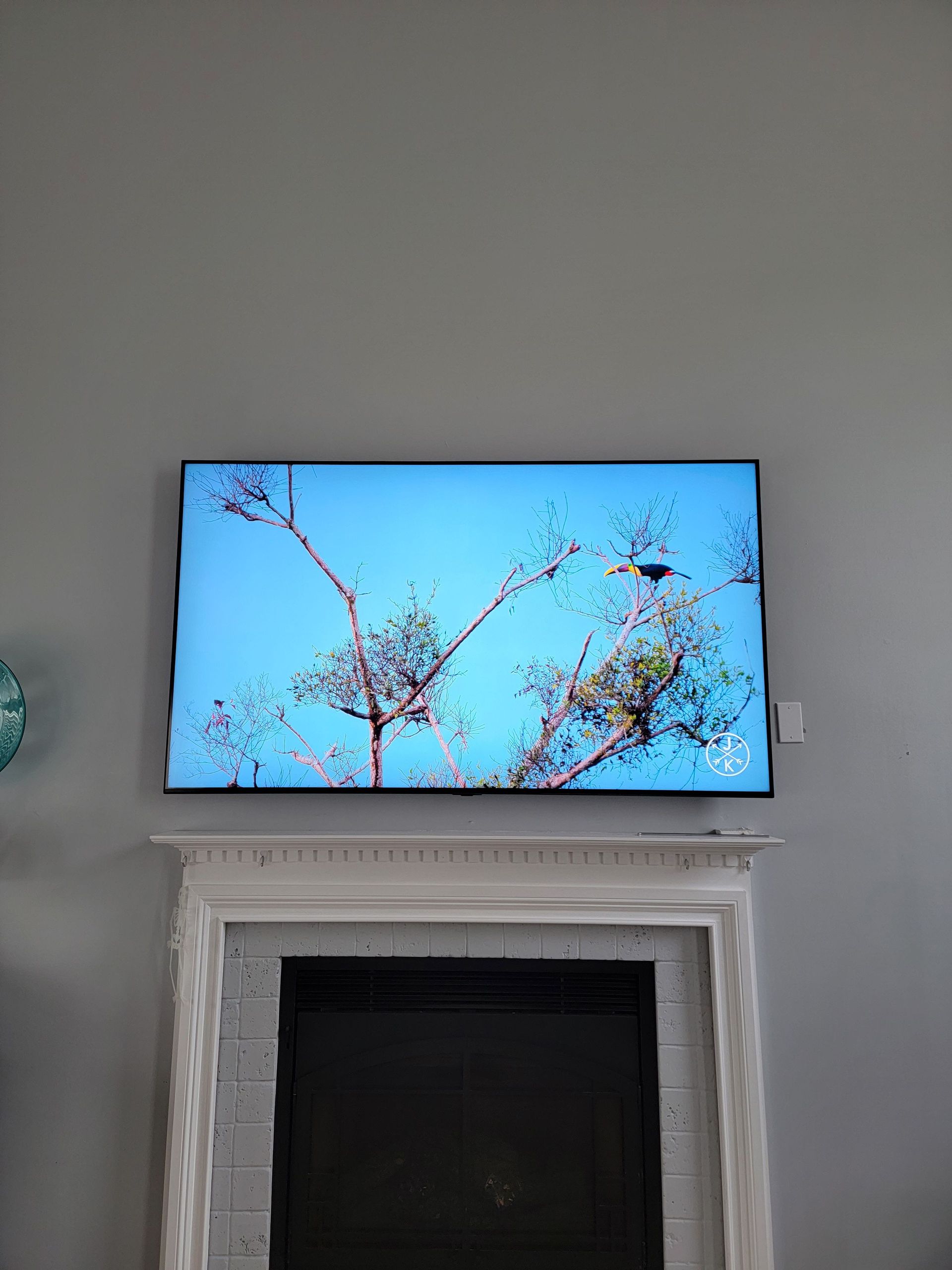 Wall-mounted TV above a fireplace displaying a tree branch scene against a blue sky by Audio Video Concepts