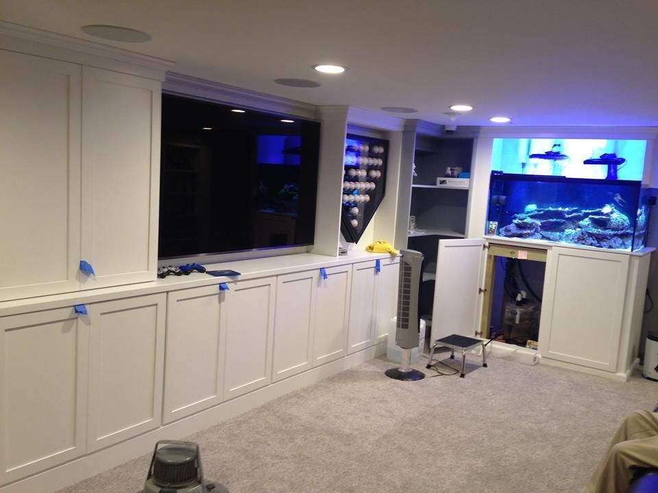 Basement room with white cabinets, carpet, and a glowing fish tank at the far end by Audio Video Concepts