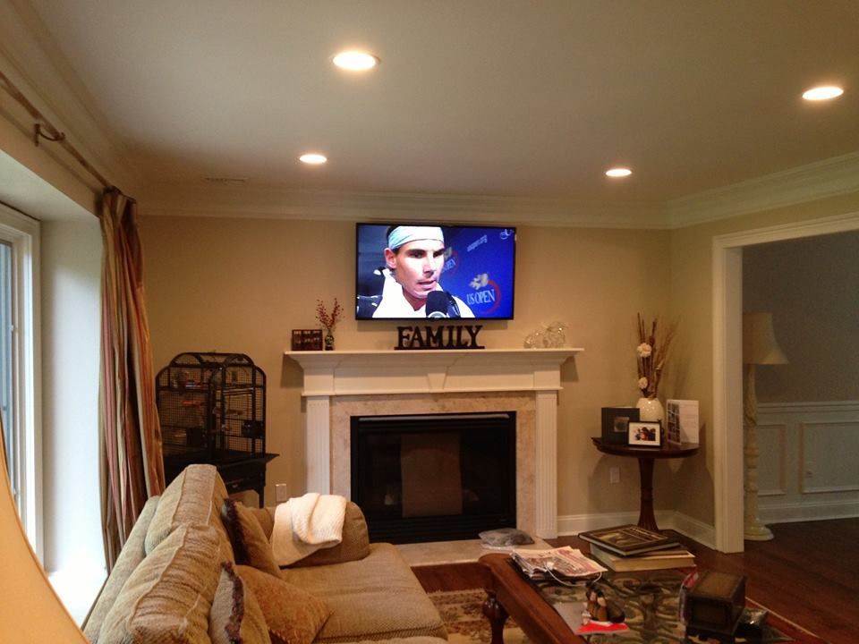 Cozy living room with fireplace, wall-mounted TV, tan couch, and warm recessed lighting  by Audio Video Concepts