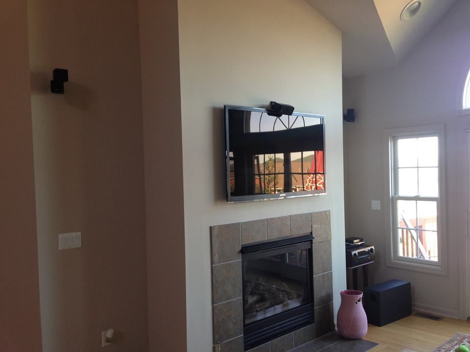 Living room with a fireplace, wall-mounted TV, and a pink vase by a glass door by Audio Video Concepts