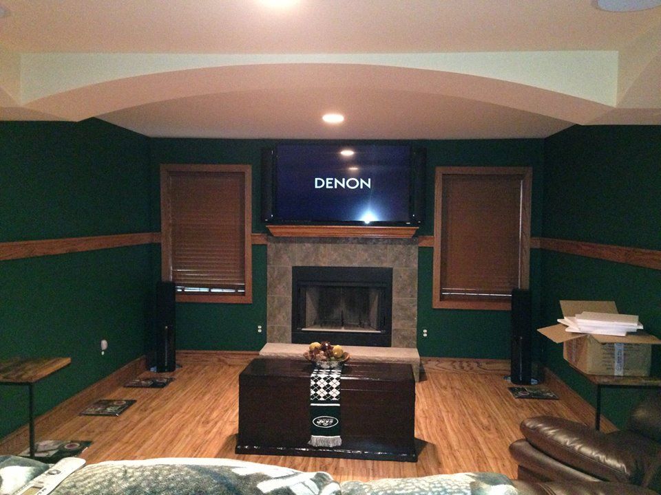 Home theater with green walls, fireplace, TV, and leather seating on a wood floor  by Audio Video Concepts