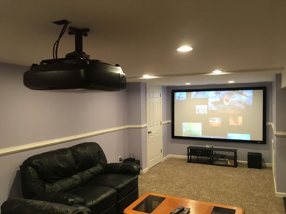 Home theater room with projector screen, leather couch, and ceiling-mounted projector by Audio Video Concepts