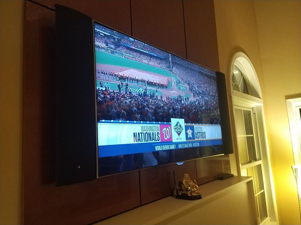 Wall-mounted TV showing a sports crowd and scoreboard in a warmly lit room by Audio Video Concepts